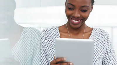 A woman in a black and white blouse, smiling while holding a tablet 